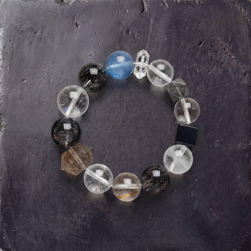 Z01 Ferro Barrier bracelet — black super seven, rutilated and clear quartz beads with one aquamarine, flat lay on dark stone